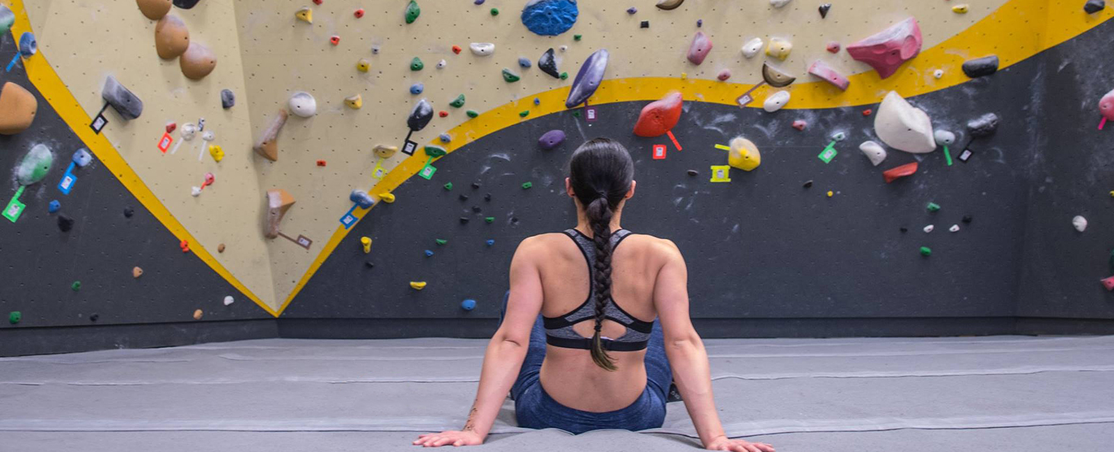person sitting on the floor in front of a rock climbing wall